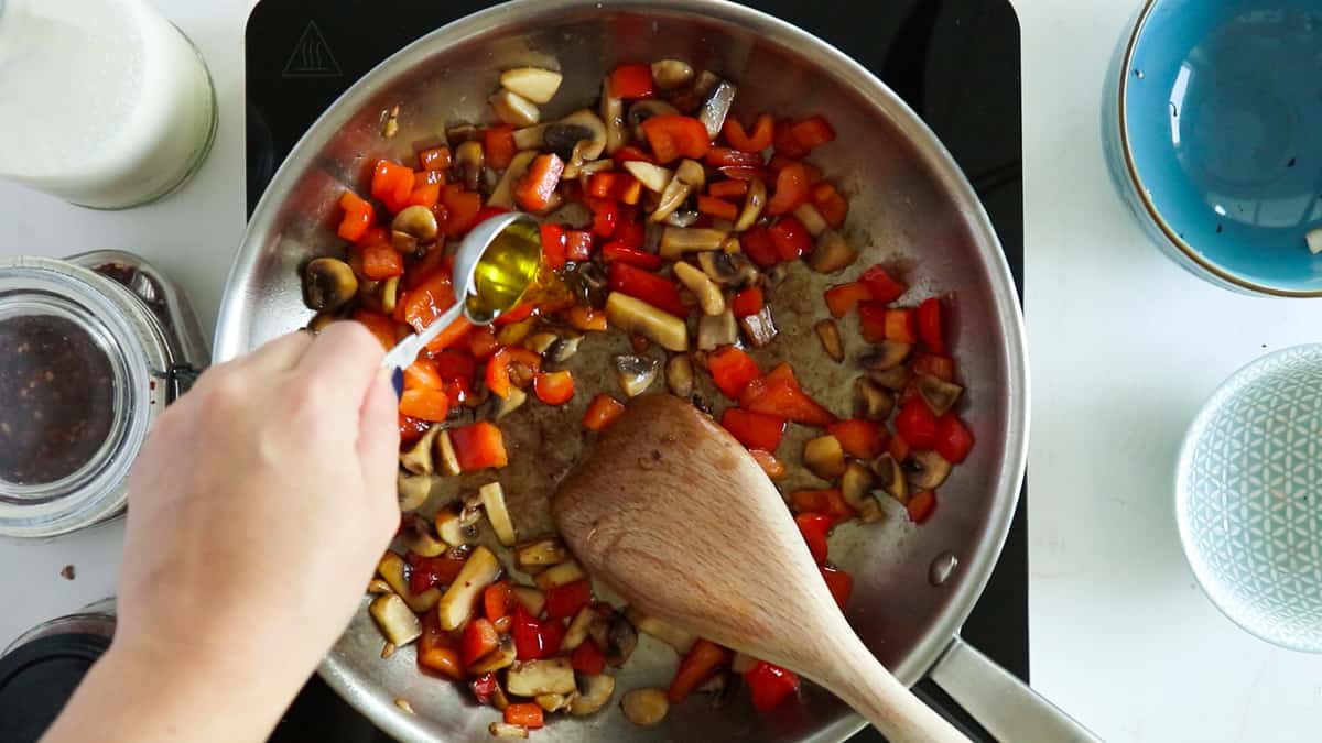 adding olive oil to mushrooms and red bell pepper