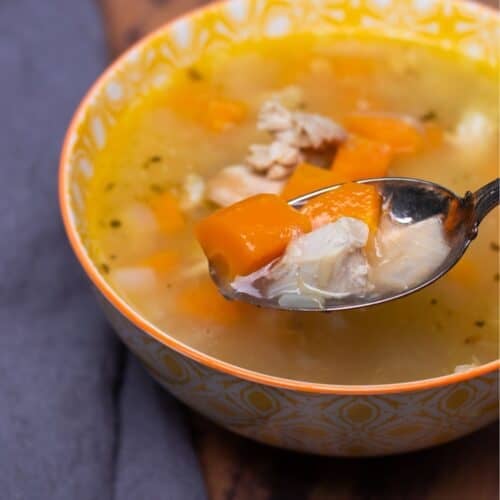 A bowl of instant pot turkey soup with a spoonful lifted out of it.