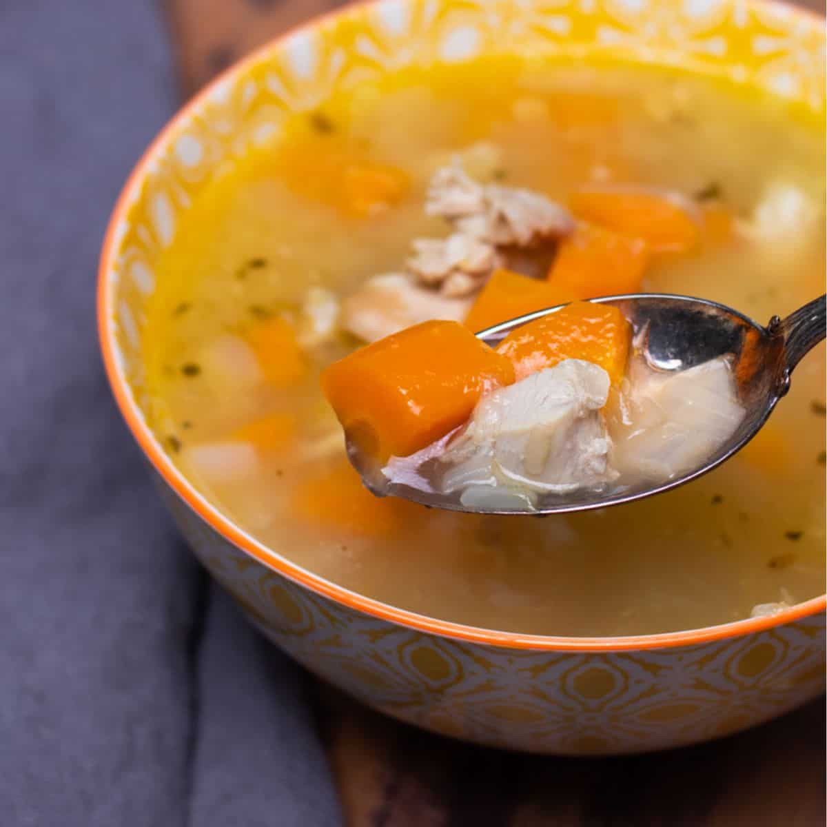 A bowl of instant pot turkey soup with a spoonful lifted out of it.