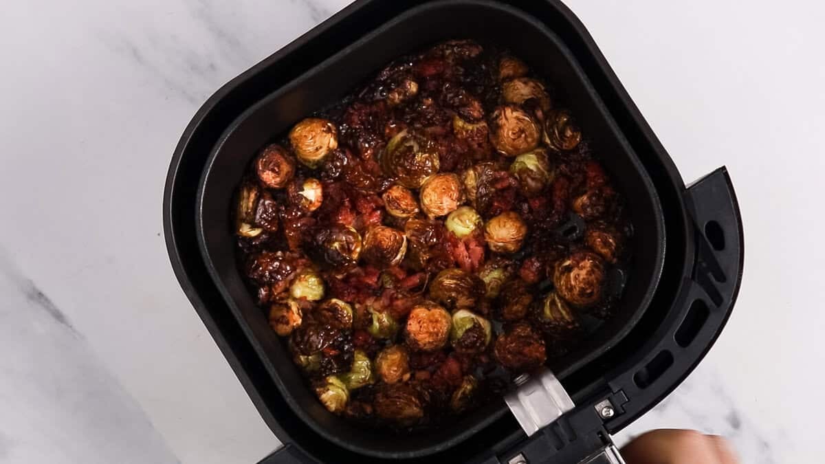 Air fryer bacon and brussels sprouts in an air fryer basket after cooking and mixing.