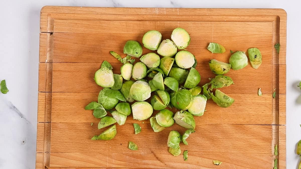 Brussels sprouts trimmed and cut in half on a chopping board.