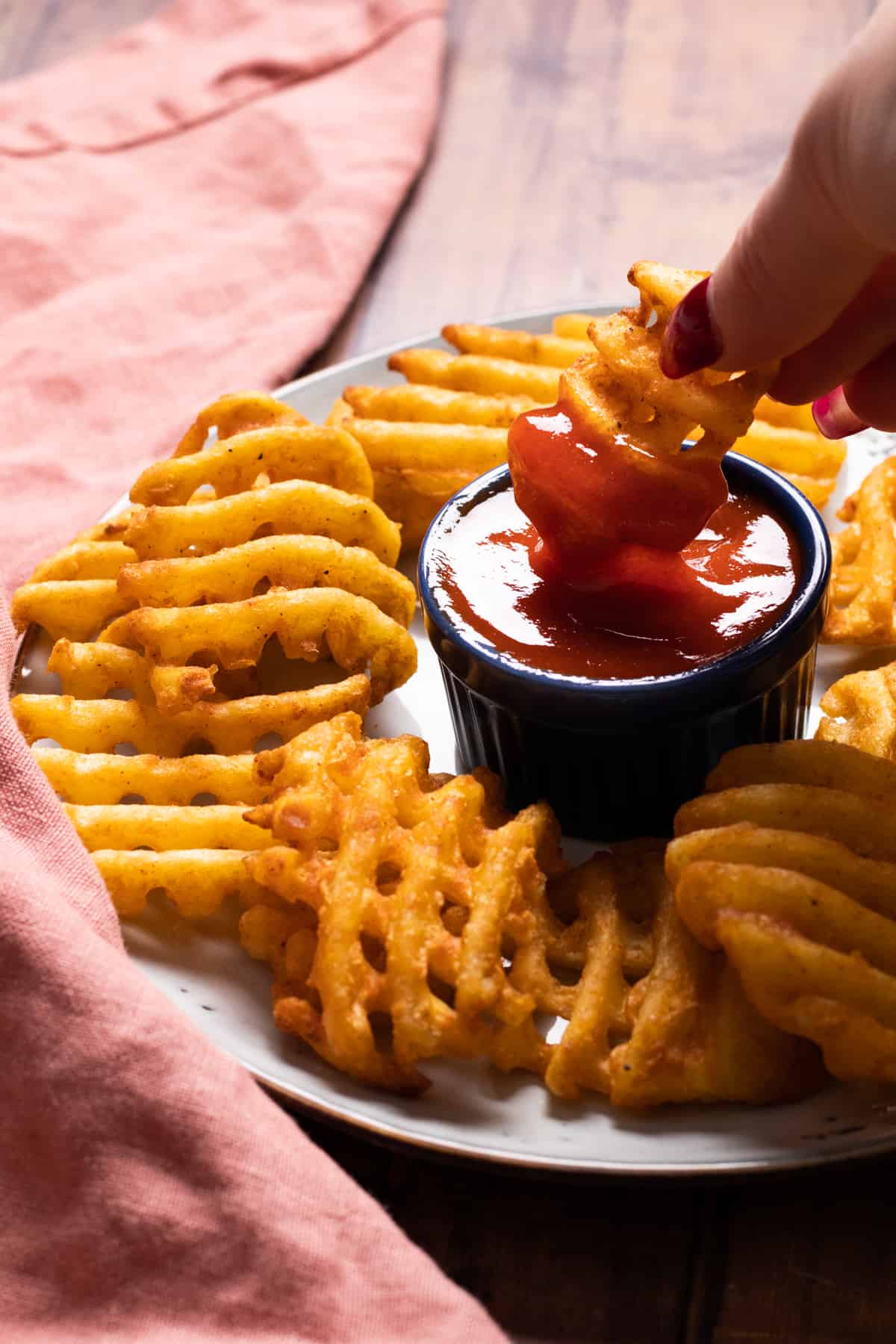 a waffle fry being dipped in red sauce.