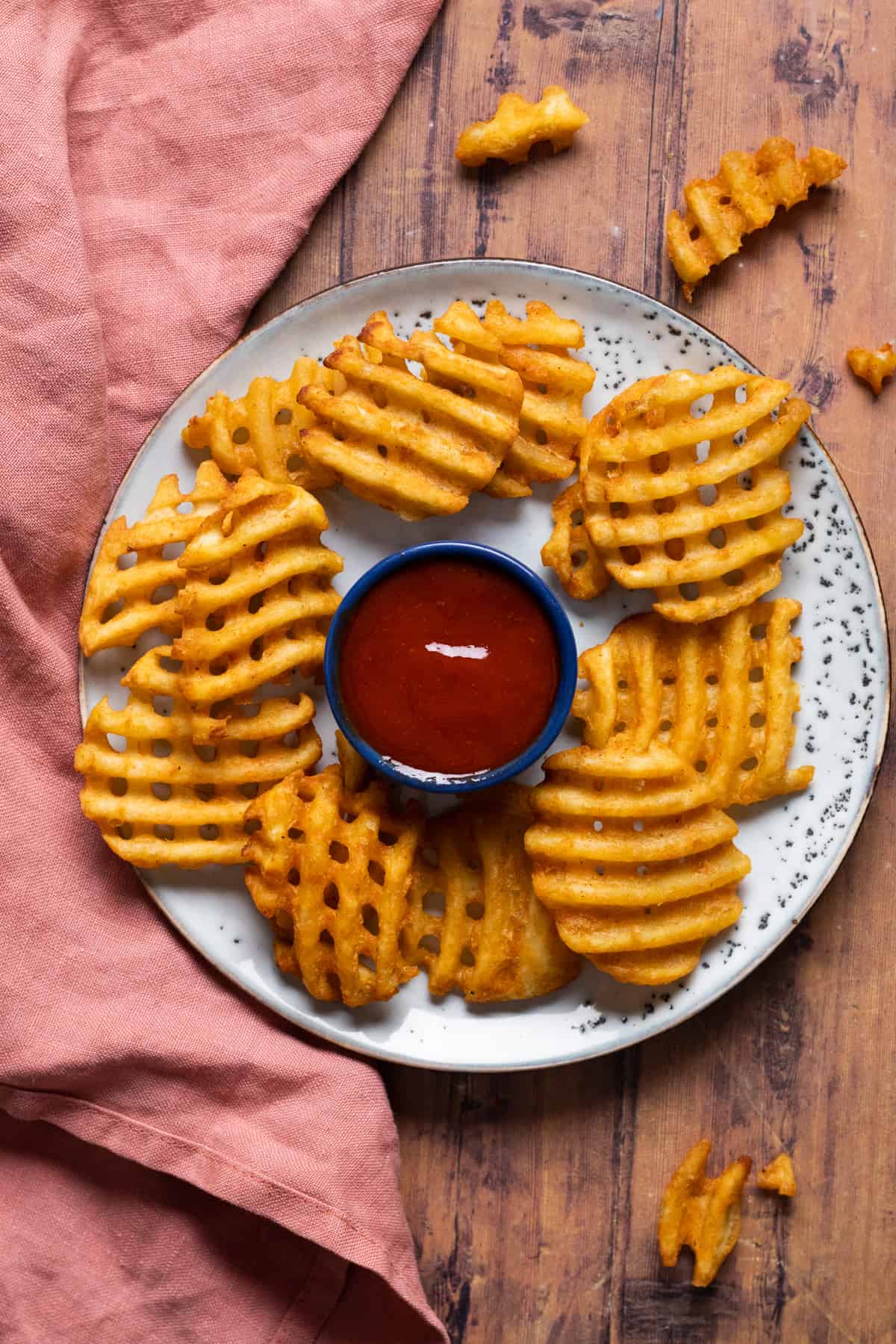 waffle fries on a blue plate with red dipping sauce.