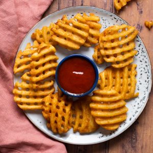 waffle fries on a blue plate with red dipping sauce.