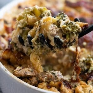 A spoonful of chicken broccoli pasta bake being lifted up out of a casserole.