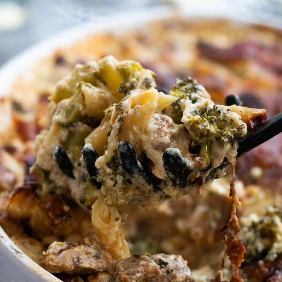 A spoonful of chicken broccoli pasta bake being lifted up from a casserole.
