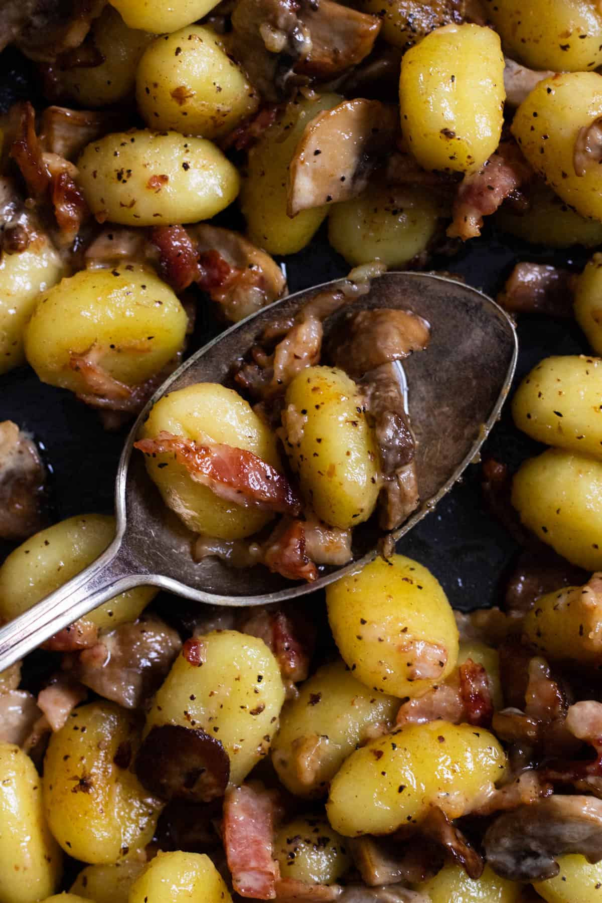 a spoonful of a pan full of creamy gnocchi with bacon and mushrooms