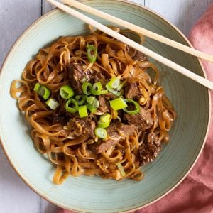 beef chow fun on a green plate with chopsticks