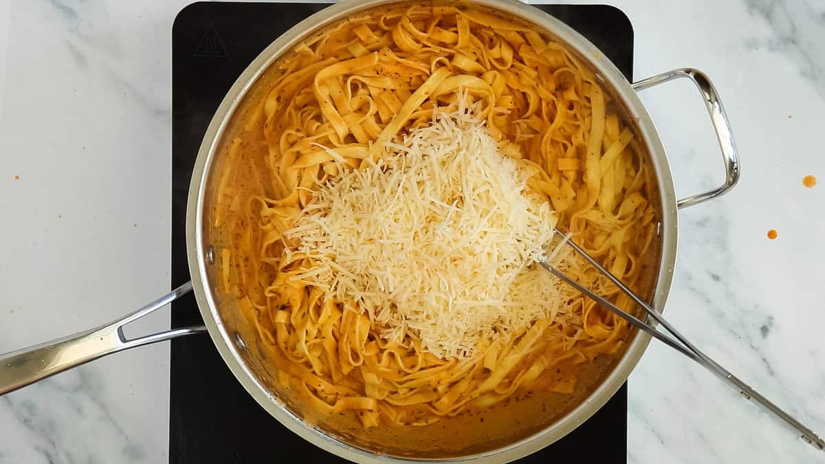Adding cheese to cajun alfredo pasta.