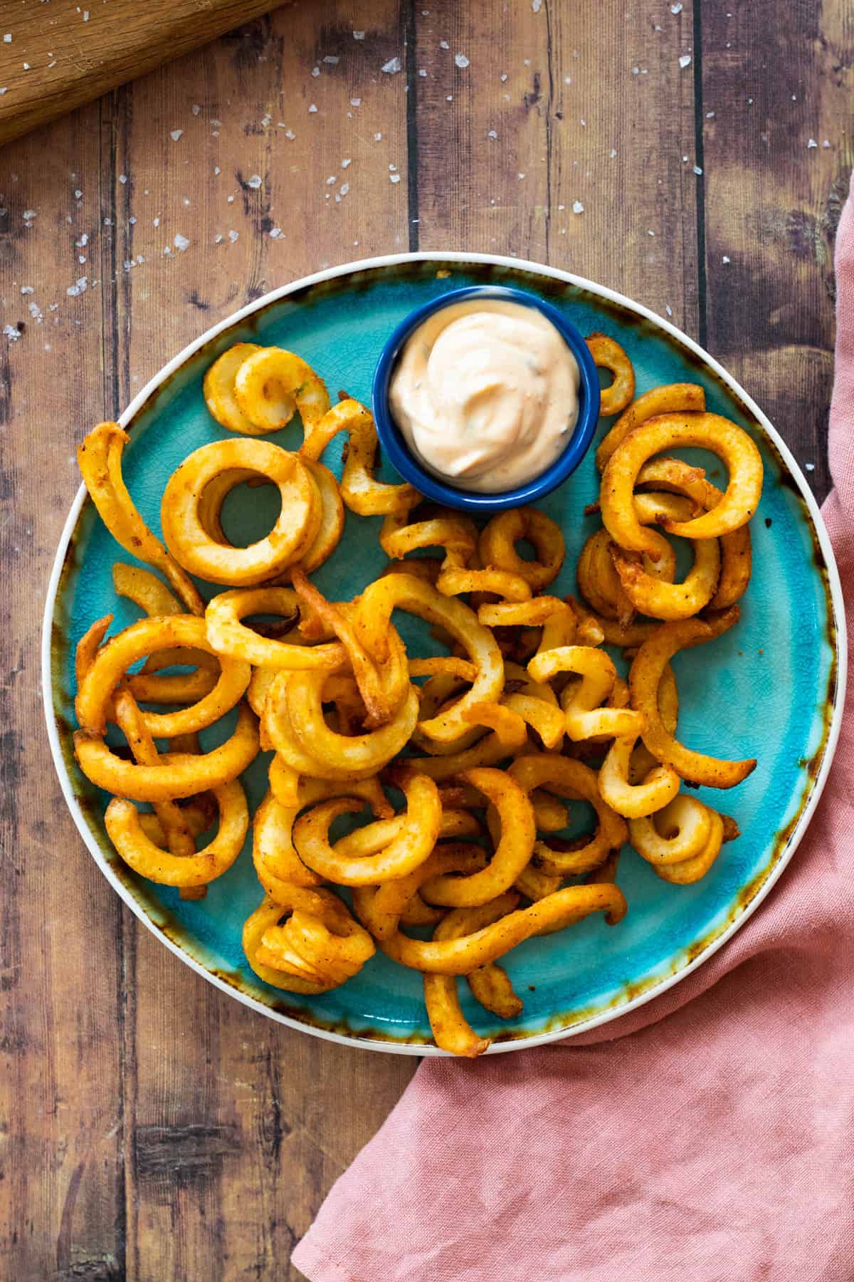 curly fries on a blue plate with a dip sauce.