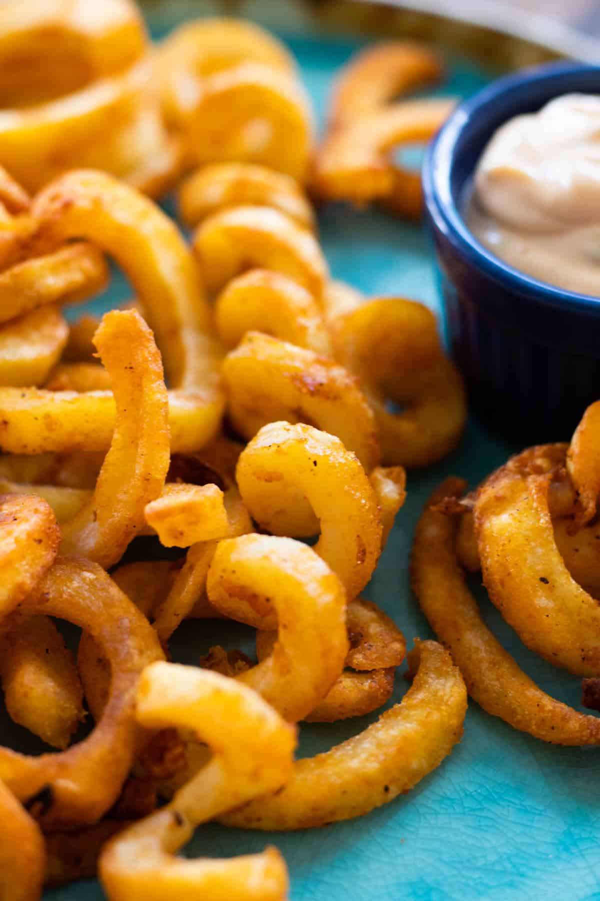 curly fries on a blue plate with a dip sauce.