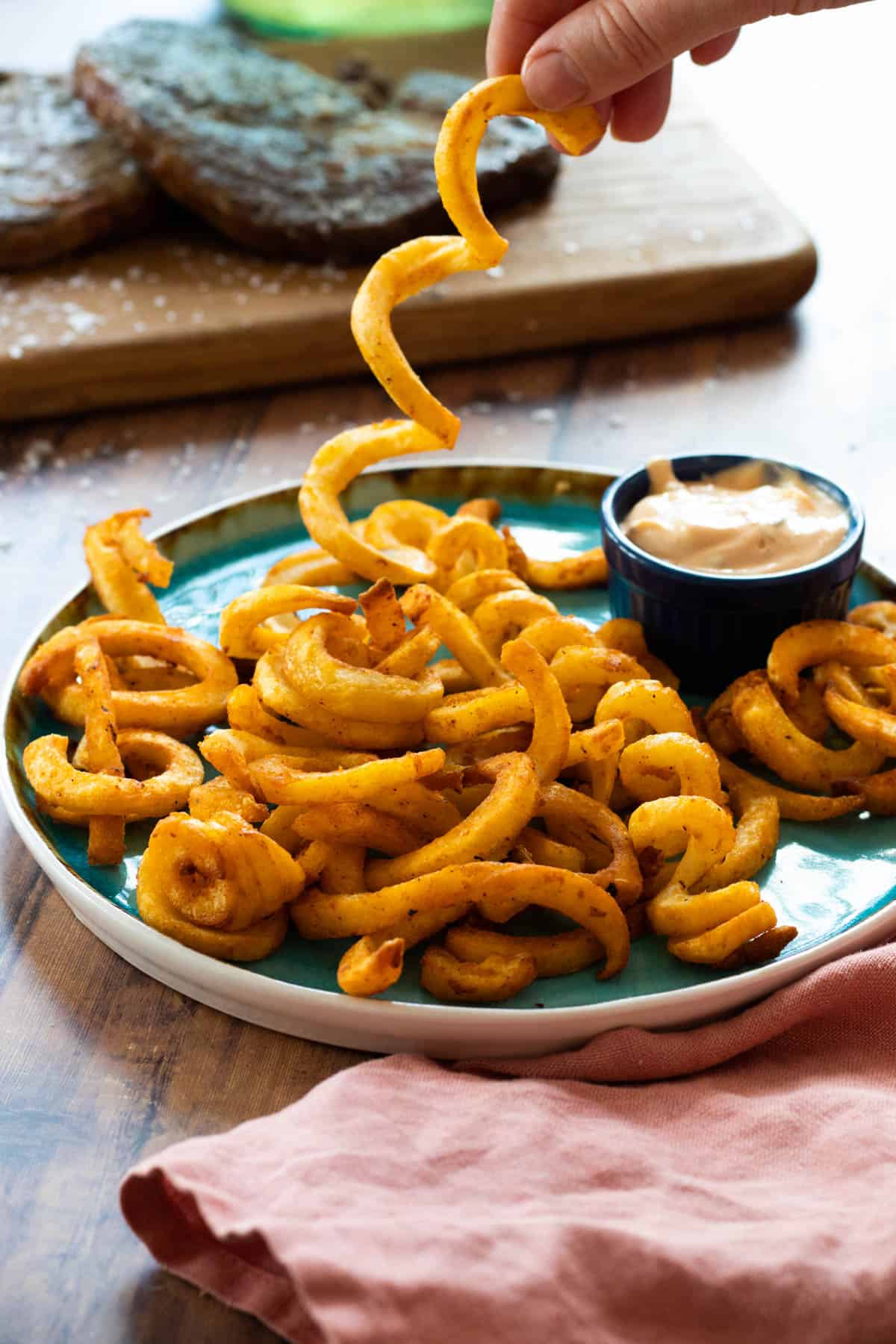 curly fries on a blue plate with a dip sauce.