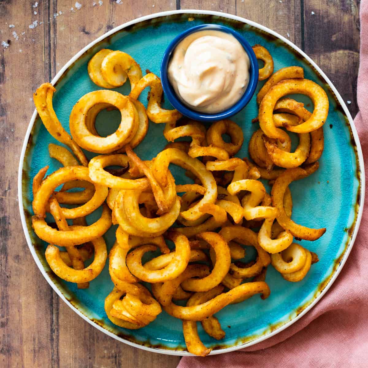 curly fries on a blue plate with a dip sauce