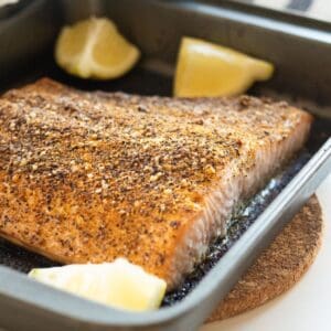Lemon pepper salmon in a non-stick pan with lemon wedges.