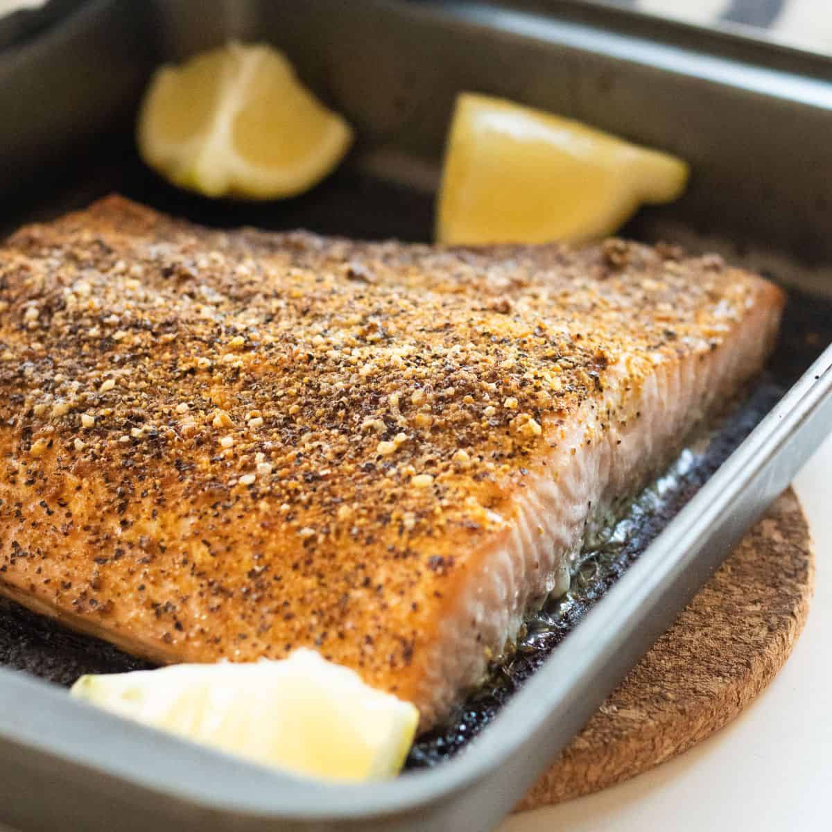 Lemon pepper salmon in a non-stick pan with lemon wedges.