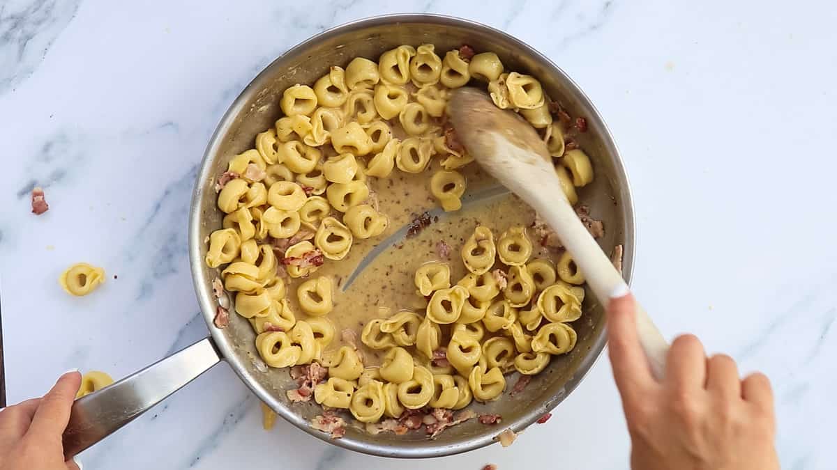 Mixing cheese paste with tortellini and pasta water.