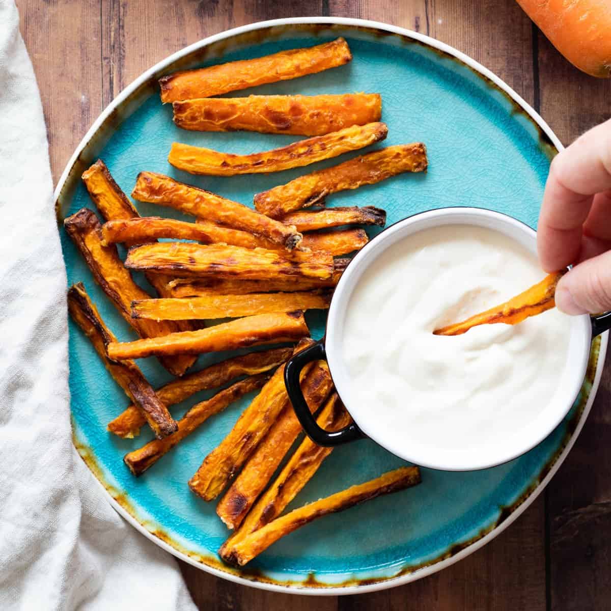 Carrot fries on a blue plate with a dipping sauce.