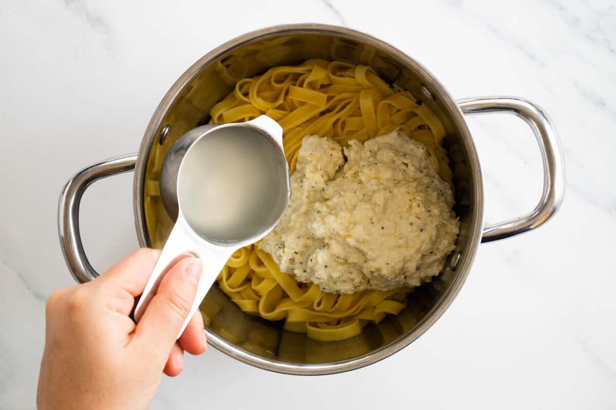 Adding pasta cooking water to a pot with pasta and lemon ricotta sauce.