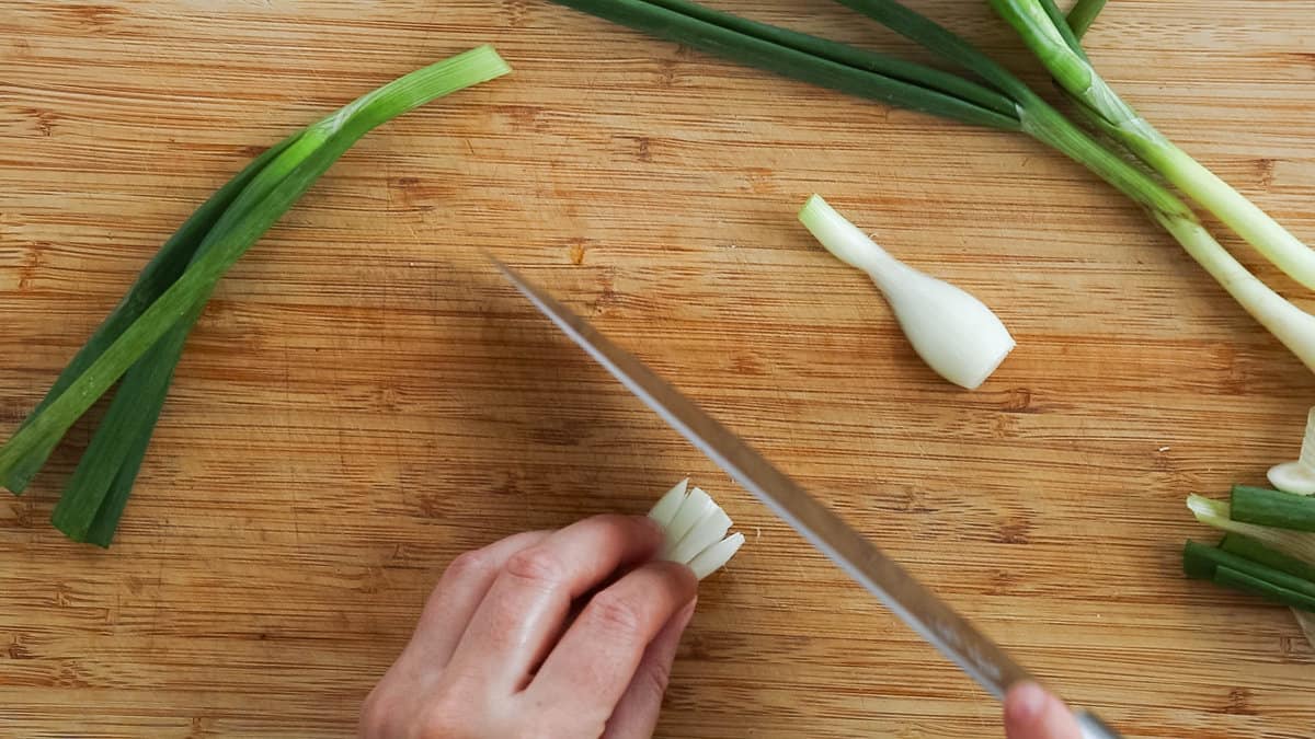 Chopping the white bulb of a green onion.