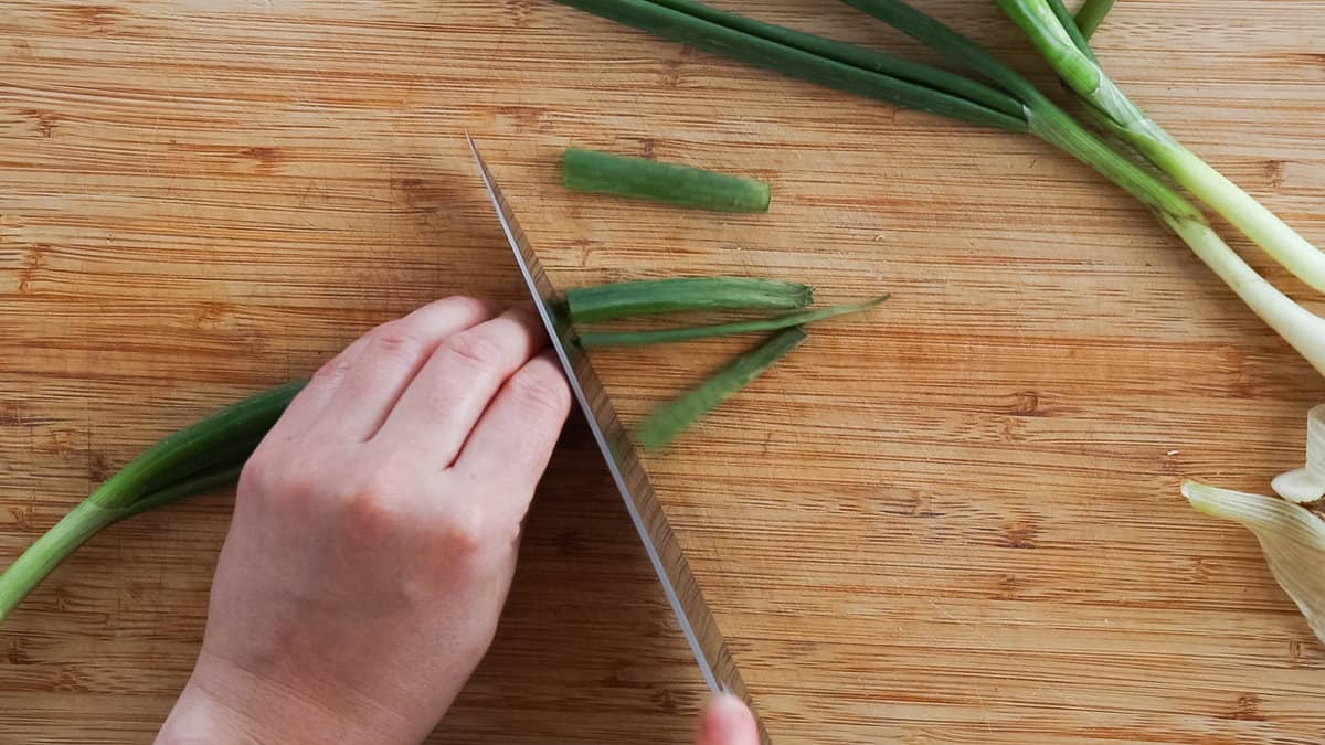 Cutting off the edge of the green tops of a green onion.