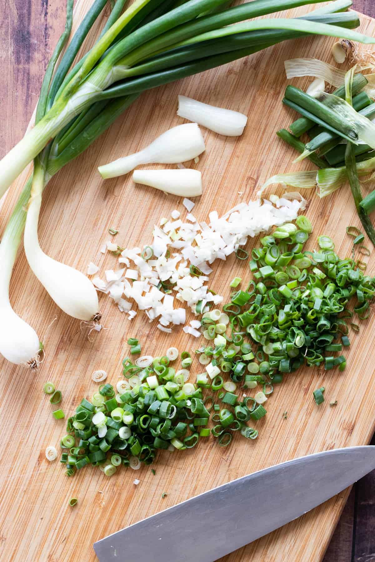 Whole and sliced green onions on a chopping board.