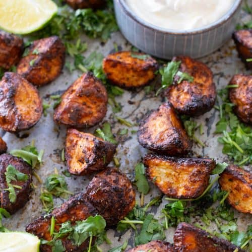 Mexican potatoes on a baking sheet with some lime wedges.