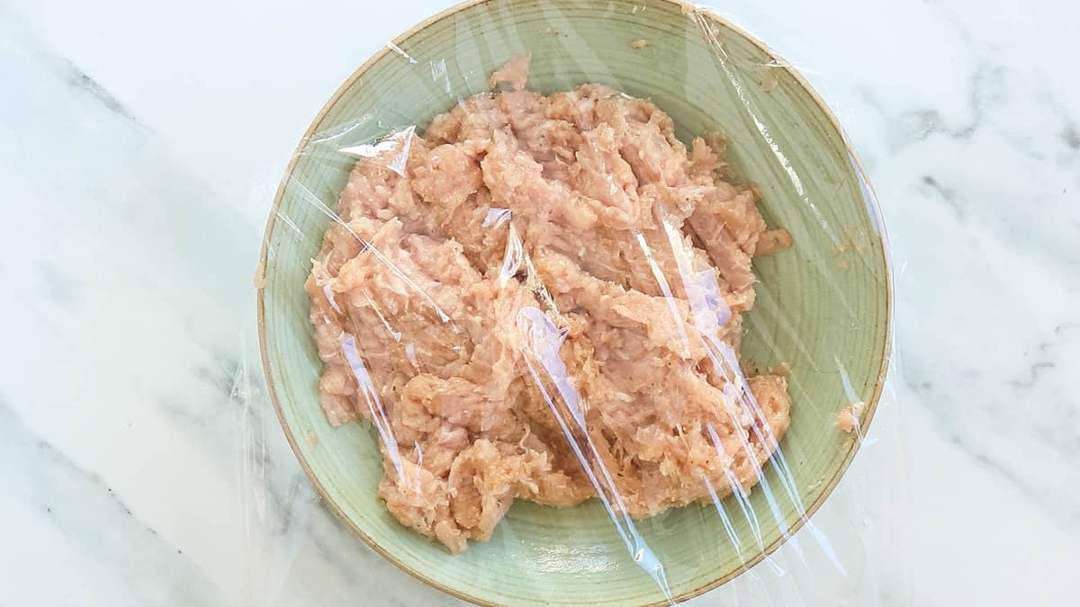 Chicken mixture in a bowl covered with plastic.