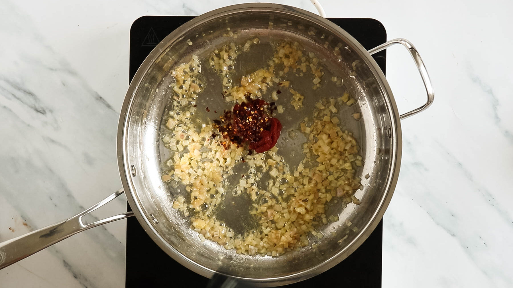 Adding tomato paste and chili flakes to skillet.
