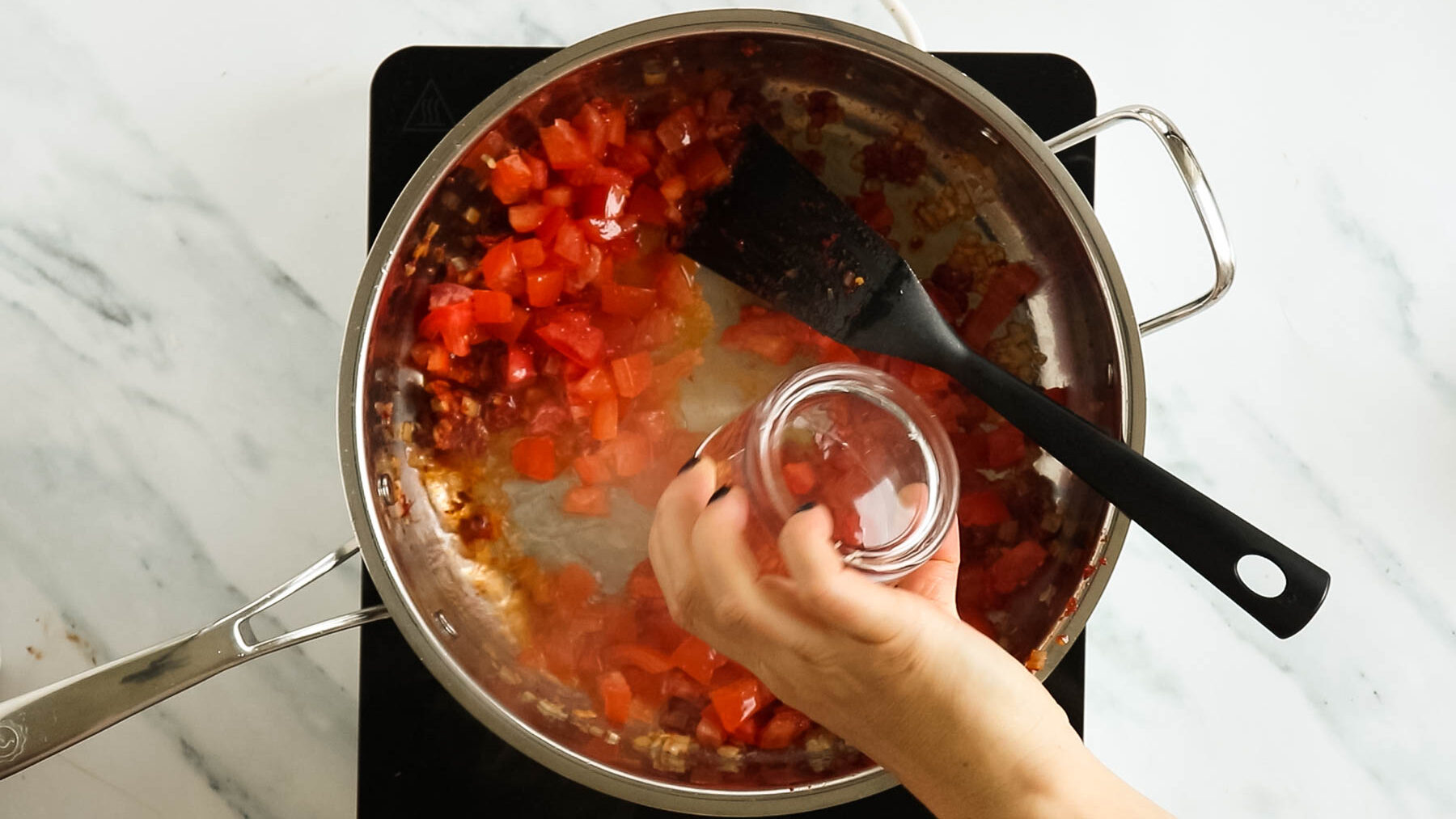 Adding vodka to tomatoes in a skillet.