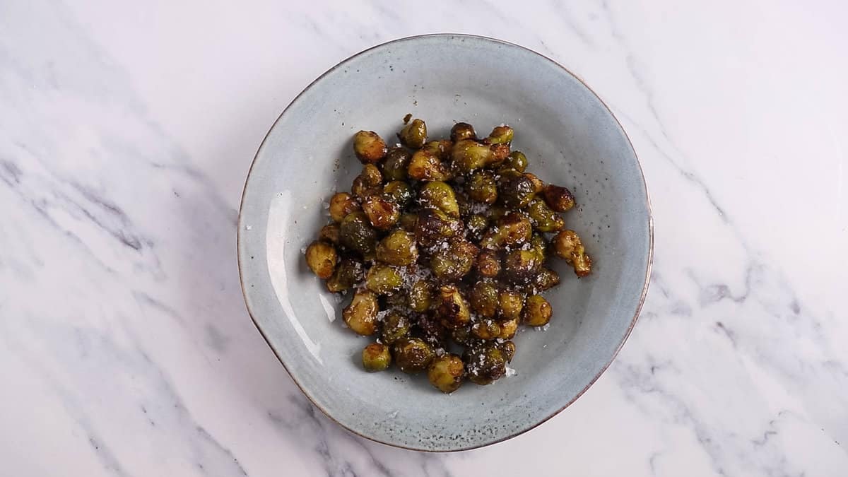 Cooked brussels sprouts topped with sea salt, in a blue bowl.