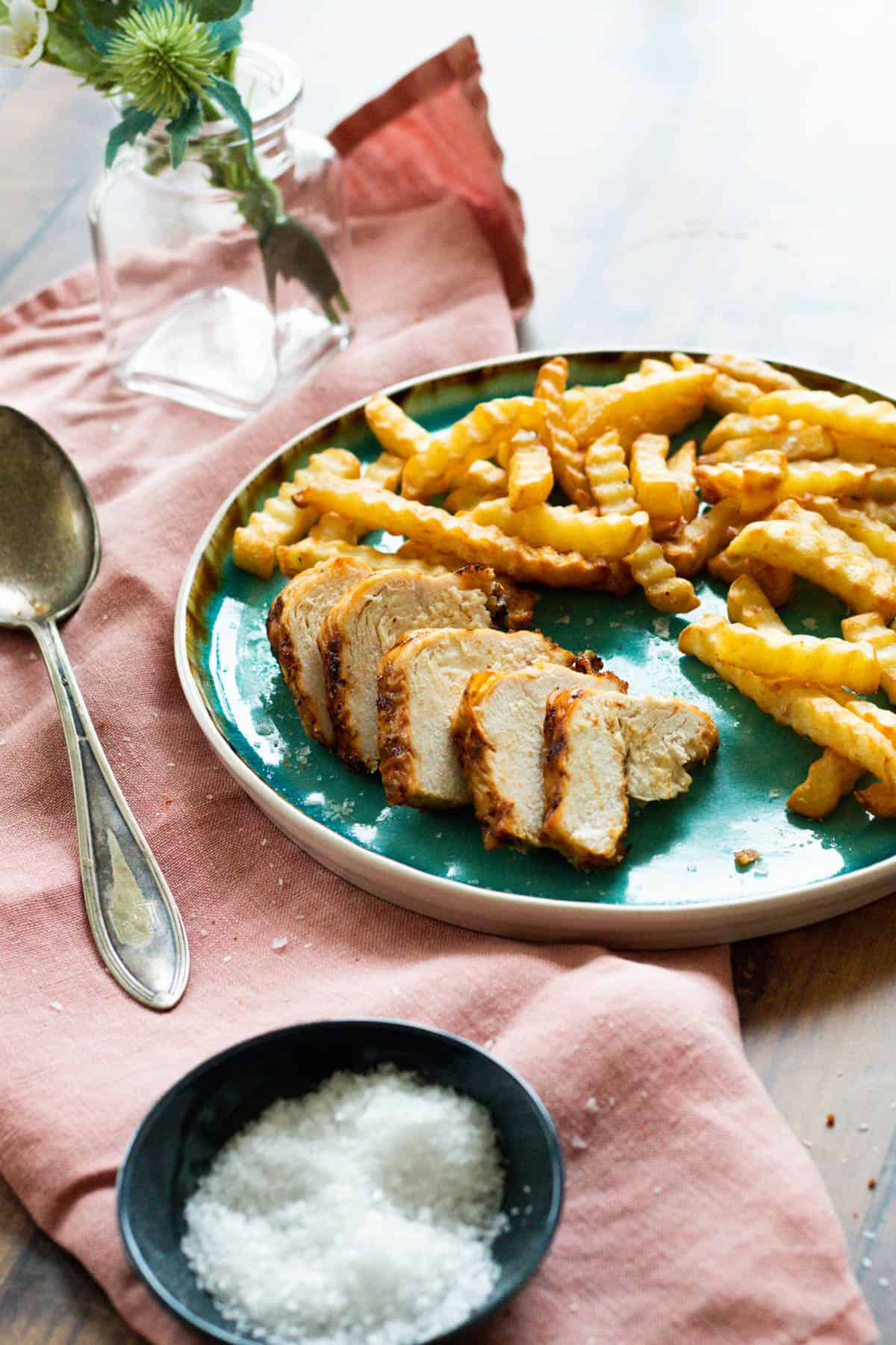 Sliced chicken breast on a blue plate with fries and sauce.