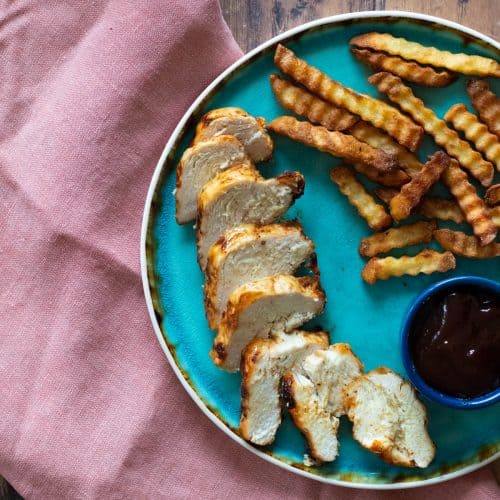 Sliced chicken breast on a blue plate with fries and sauce.