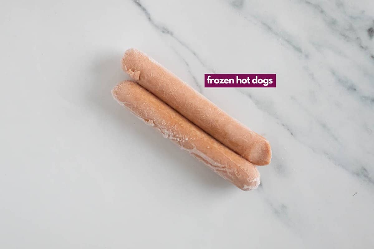 Two frozen hot dogs on a marble countertop.