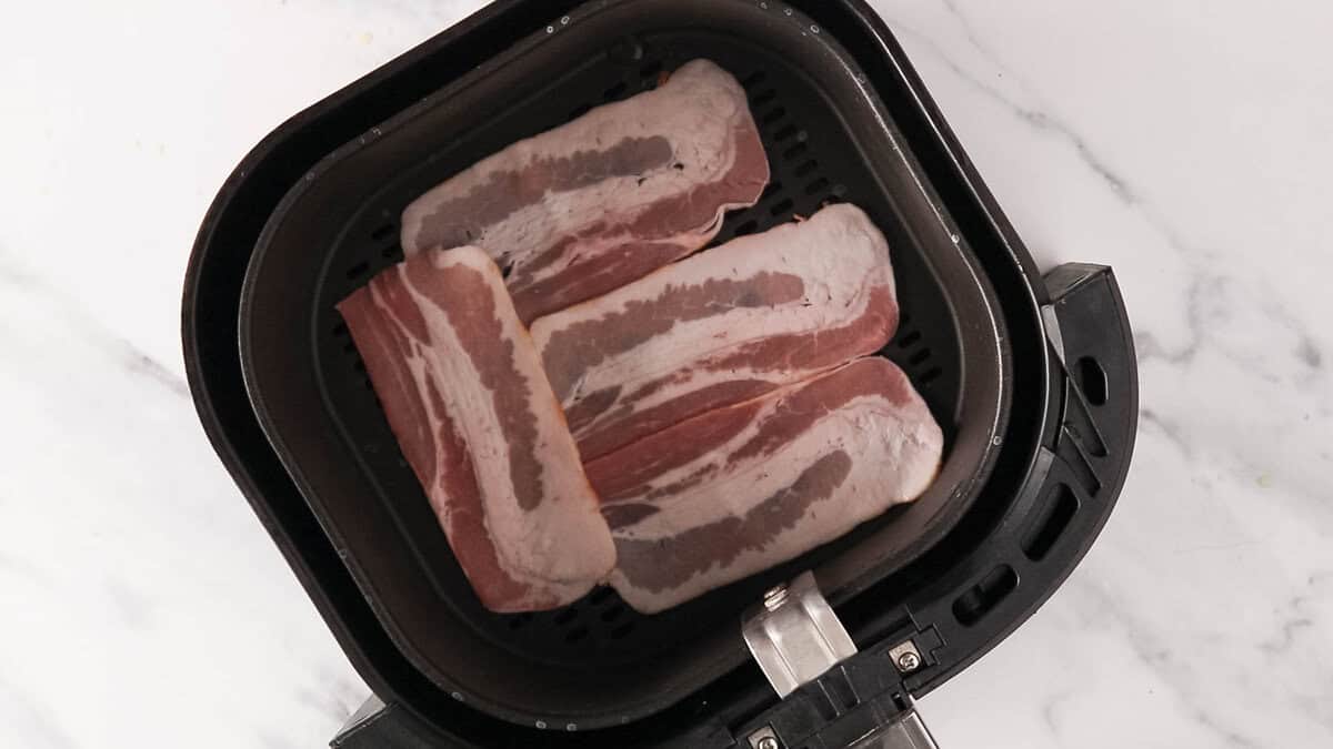 Raw bacon slices placed in an air fryer.
