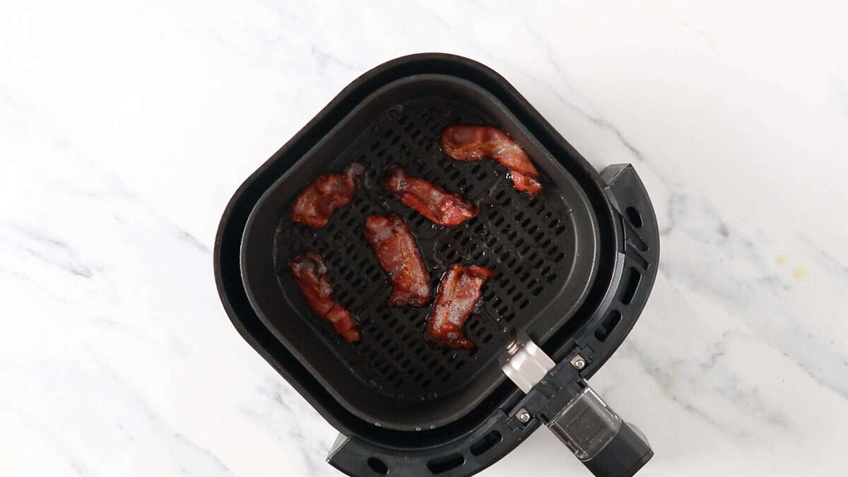 Cooked bacon slices in an air fryer basket.