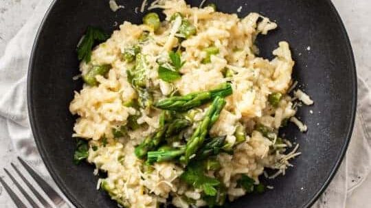 Asparagus risotto on a black plate.