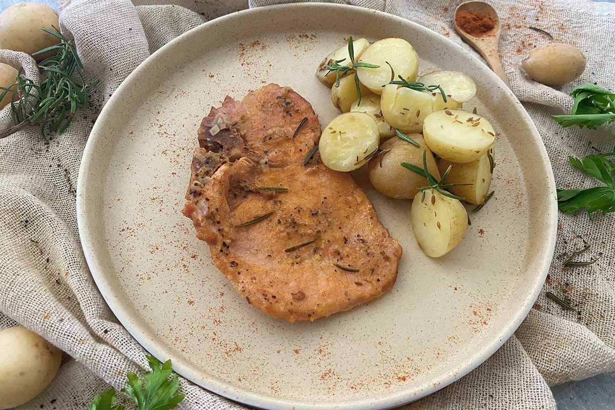 A pork chop on a plate with potatoes.