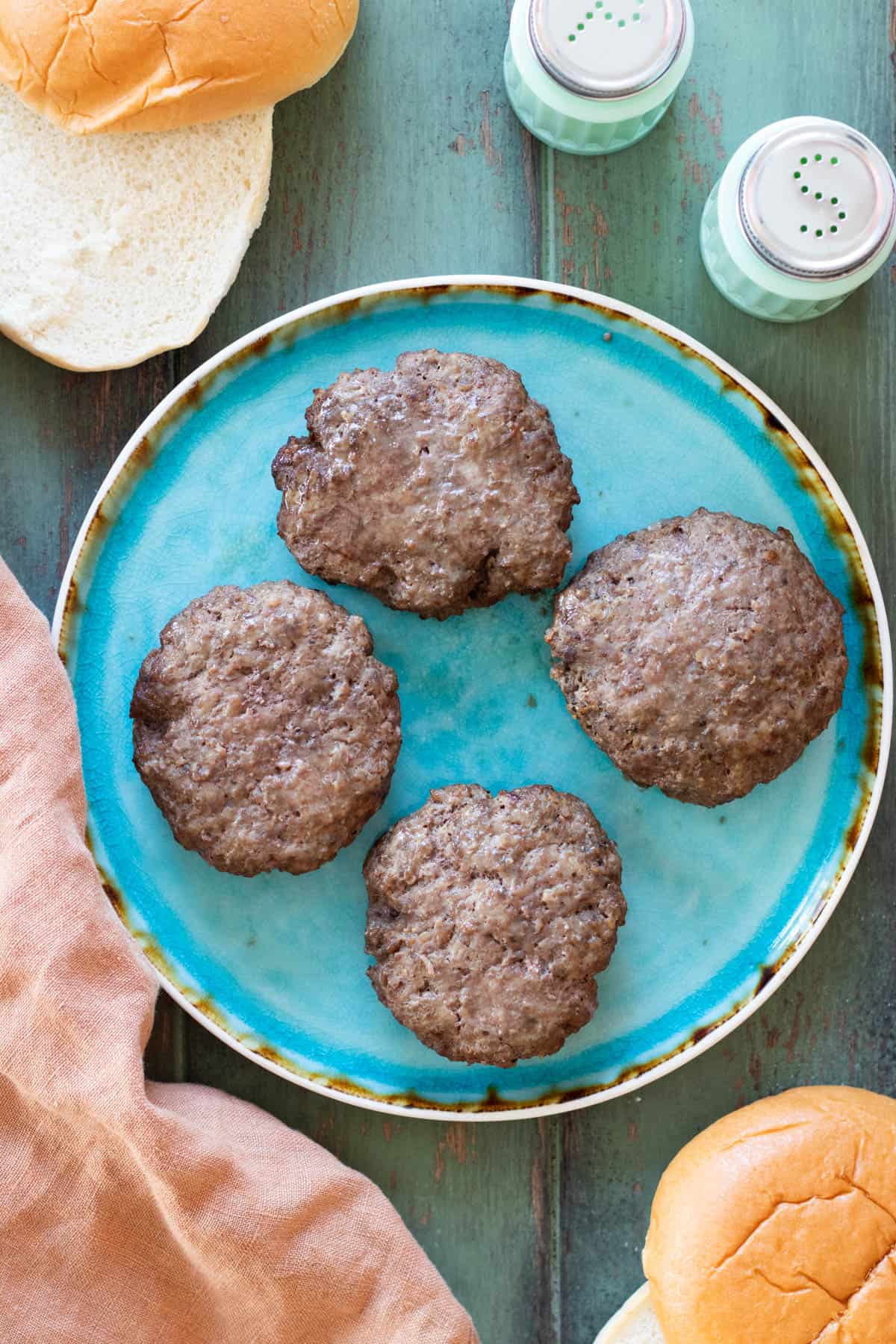 Four hamburger patties on a blue plate after air frying.