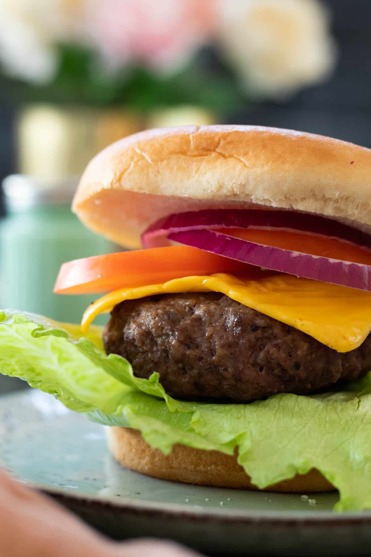 Air fryer hamburger in a bun topped with cheese and vegetables.