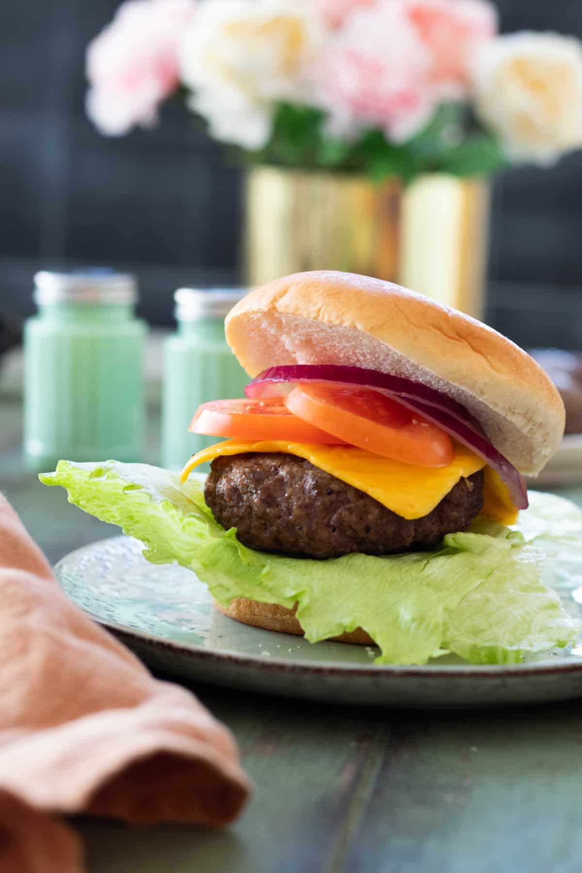 Air fryer hamburger in a bun topped with cheese and vegetables.