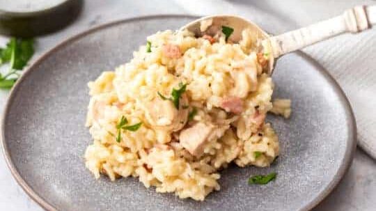 Chicken and bacon risotto being spooned onto a plate.