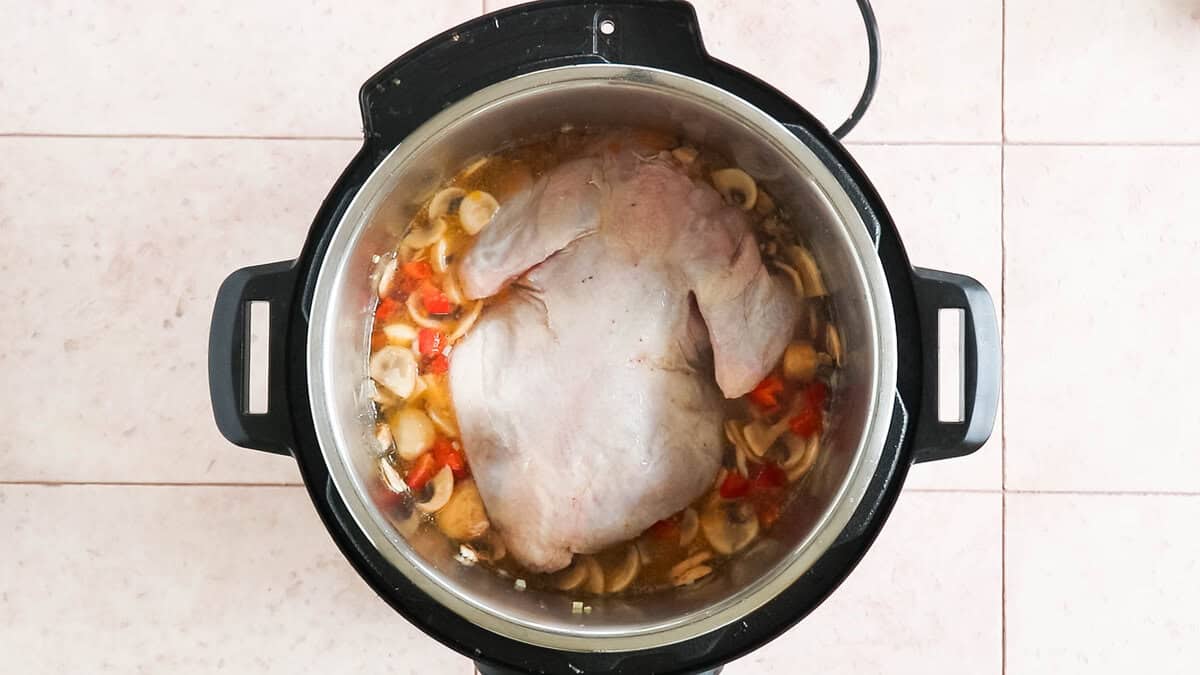 A chicken with water and other ingredients in an instant pot before cooking to make chicken soup.