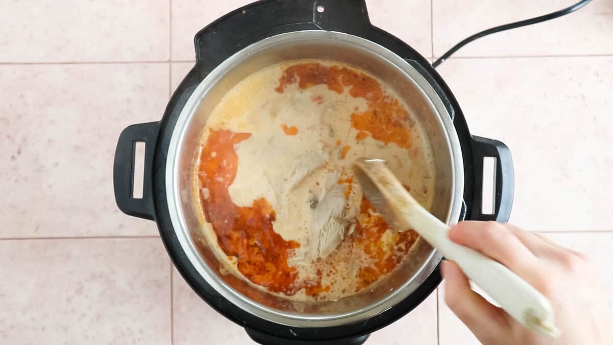 Mixing in shredded chicken with chicken soup base to make chicken soup.