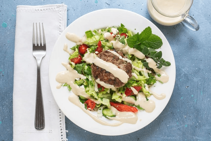 A plate with salad, a lamb burger, and dressing.