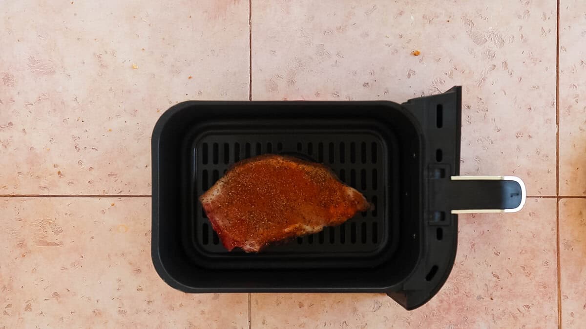 A bone in pork chop placed in an air fryer basket for cooking.