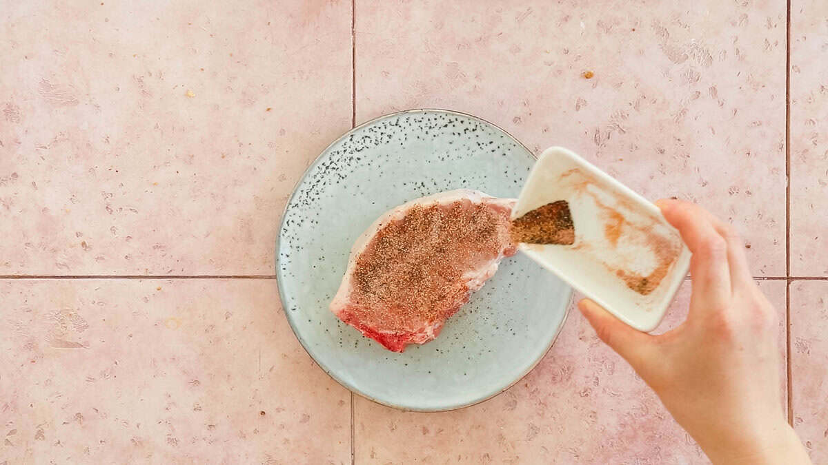 Seasoning a bone in pork chop before cooking it in the air fryer.