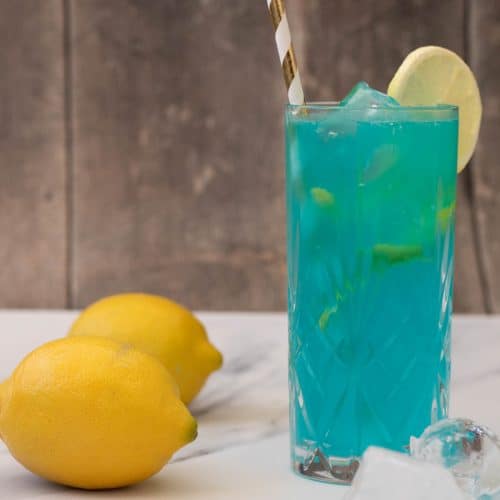 A blue lagoon mocktail next to some lemons.