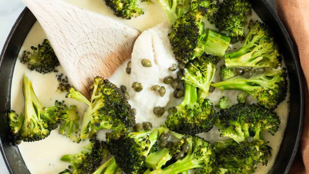 A skillet full of fish and broccoli in lemon caper sauce.