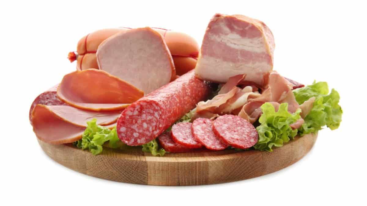 Assortment of delicious deli meats on wooden board, isolated on white