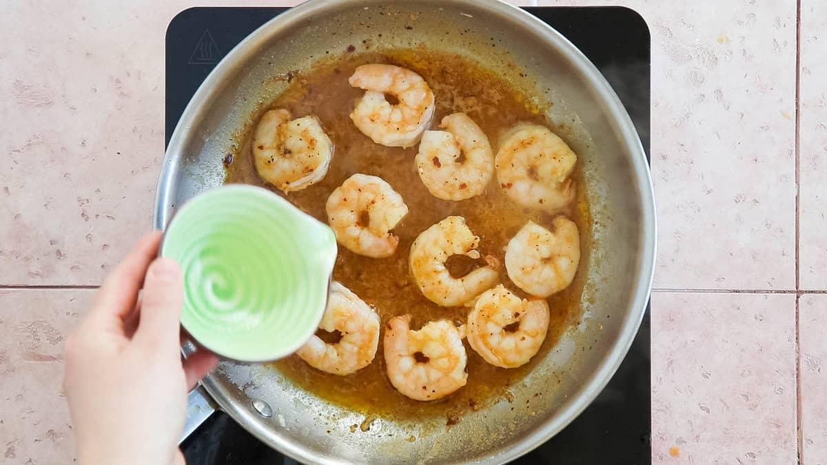 Adding lemon juice to a pan with cooked shrimp in sauce.